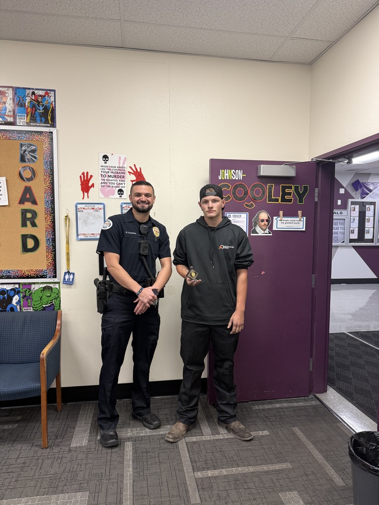 Two men stand next in a classroom. One wears a police uniform. The other holds an award.