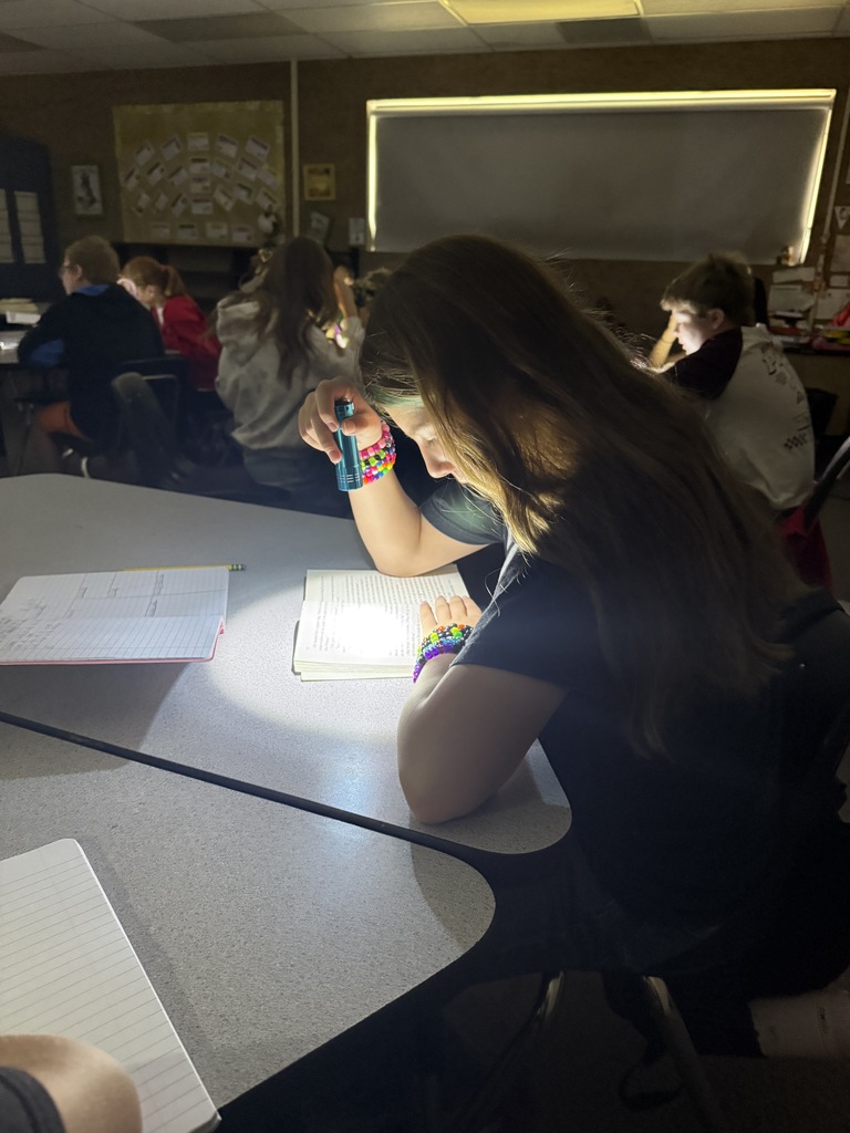 a picture of a student at a table reading with a flashlight