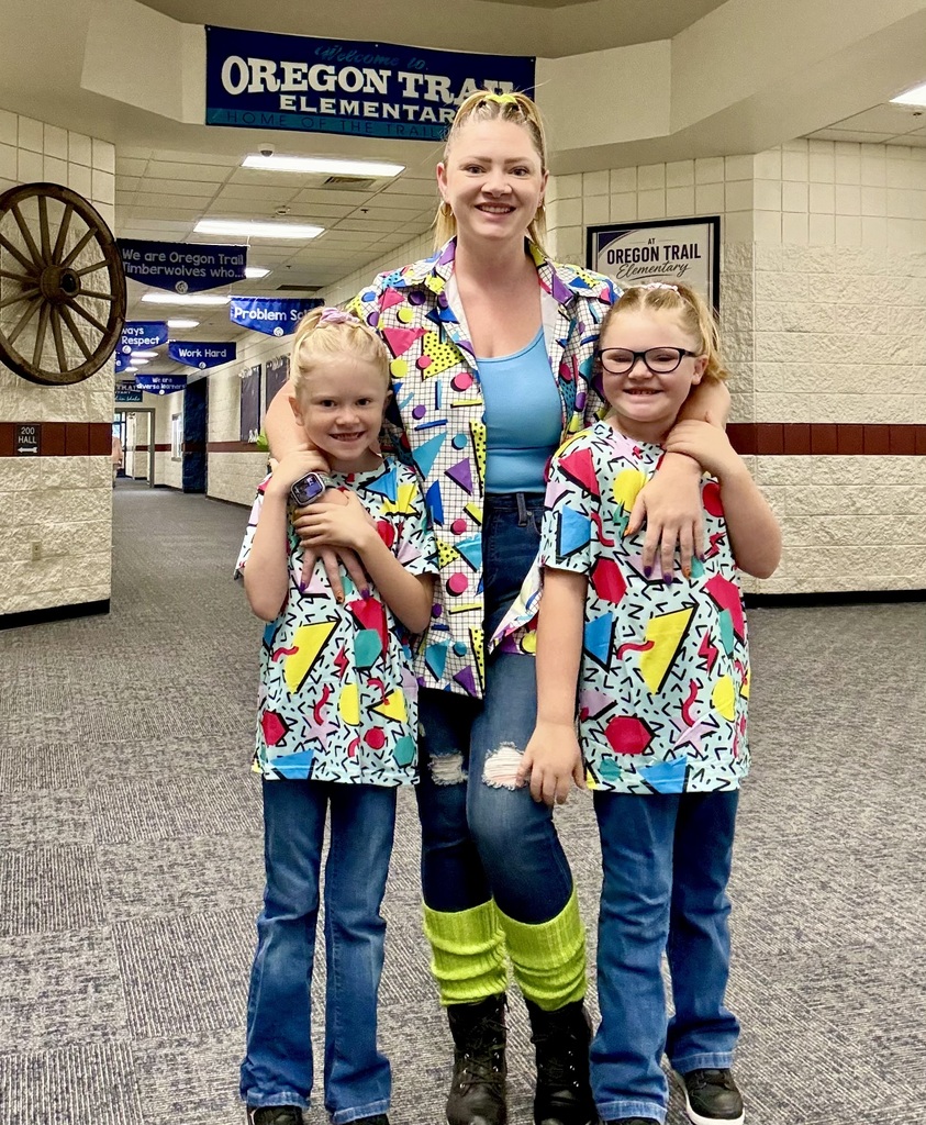 A woman and two children in matching colorful tops and jeans stand close together in a corridor.