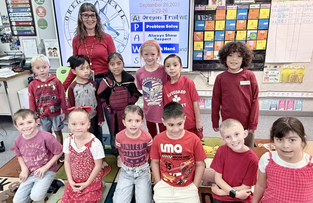 A classroom with children and a teacher. They are smiling and posing for a group photo.