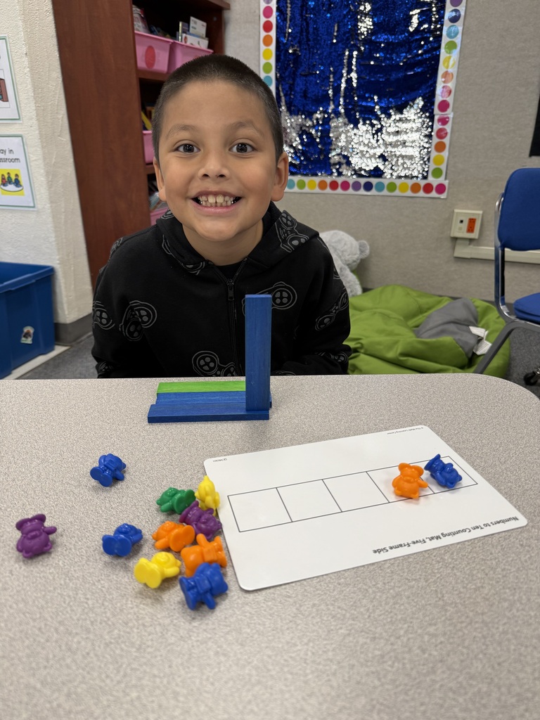 A young child sits at a table with a colorful game board. Multiple colored tokens are scattered across the board.
