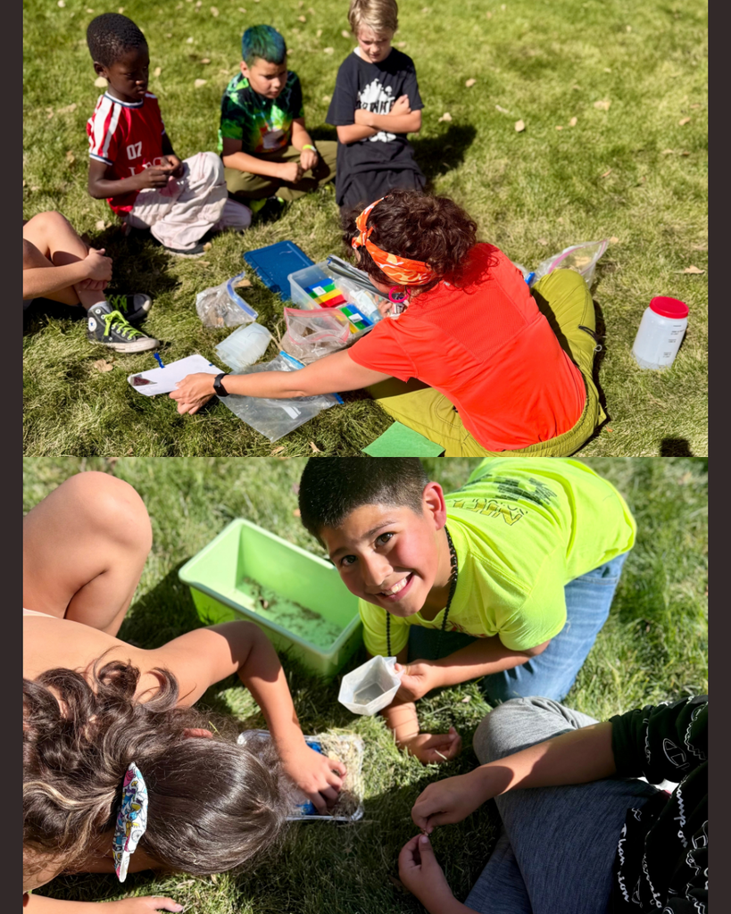 Several children and an adult sit on grass. They are using a container of water for an activity.