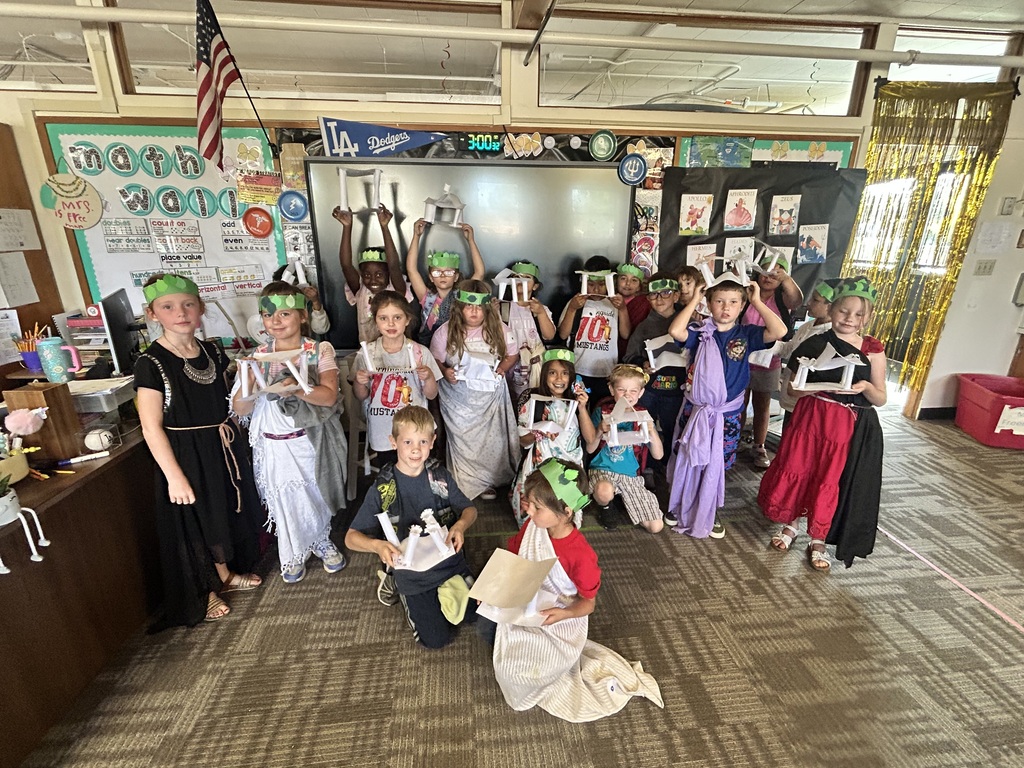 A classroom full of children wearing costumes, some with headbands, holding props, and posing for a picture.