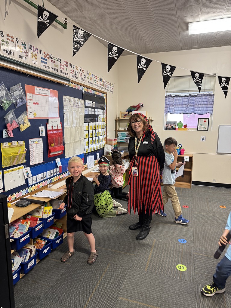 A classroom with a pirate theme. A woman in pirate attire stands in the middle. Kids in costumes play.