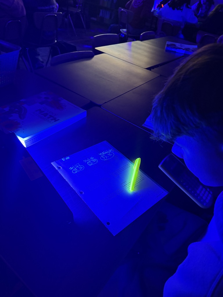 A person is seated at a table in a dark room. They have a notebook with a bright yellow highlighter on it.