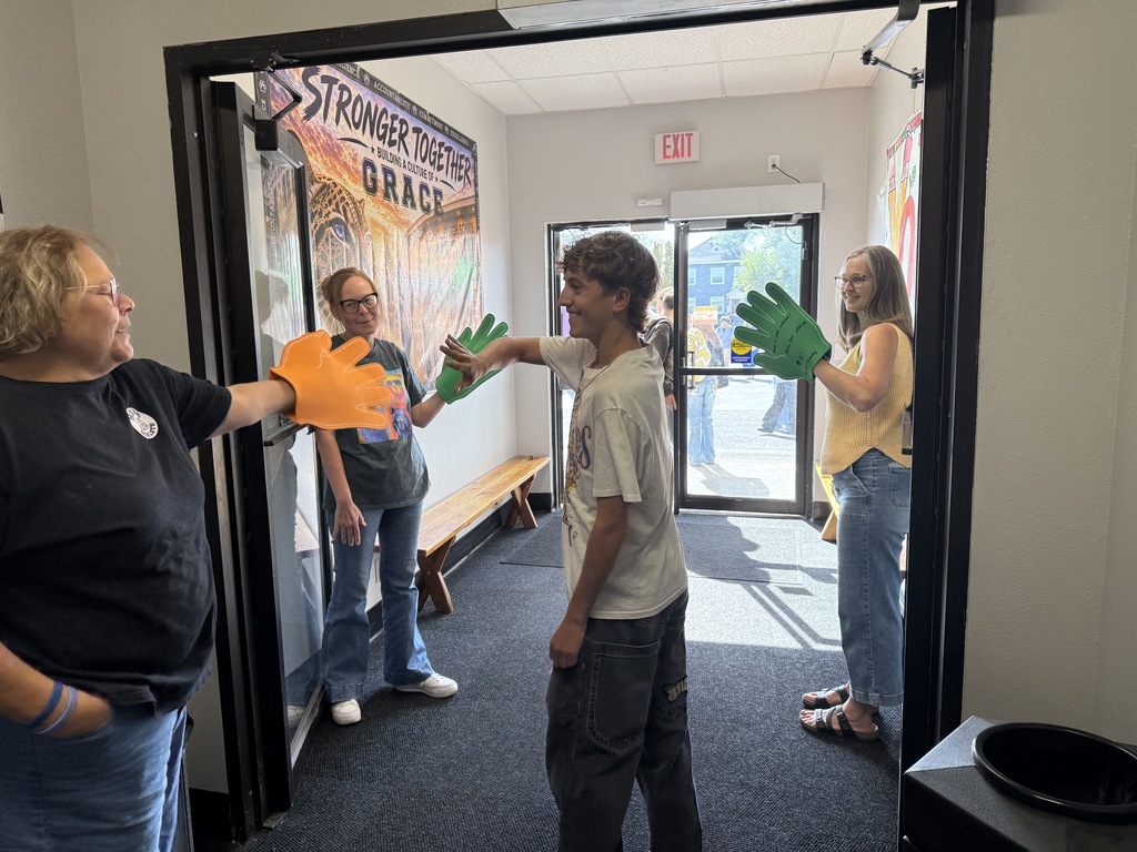 Four people face each other with hands in green gloves, two in the hallway, two in the room.