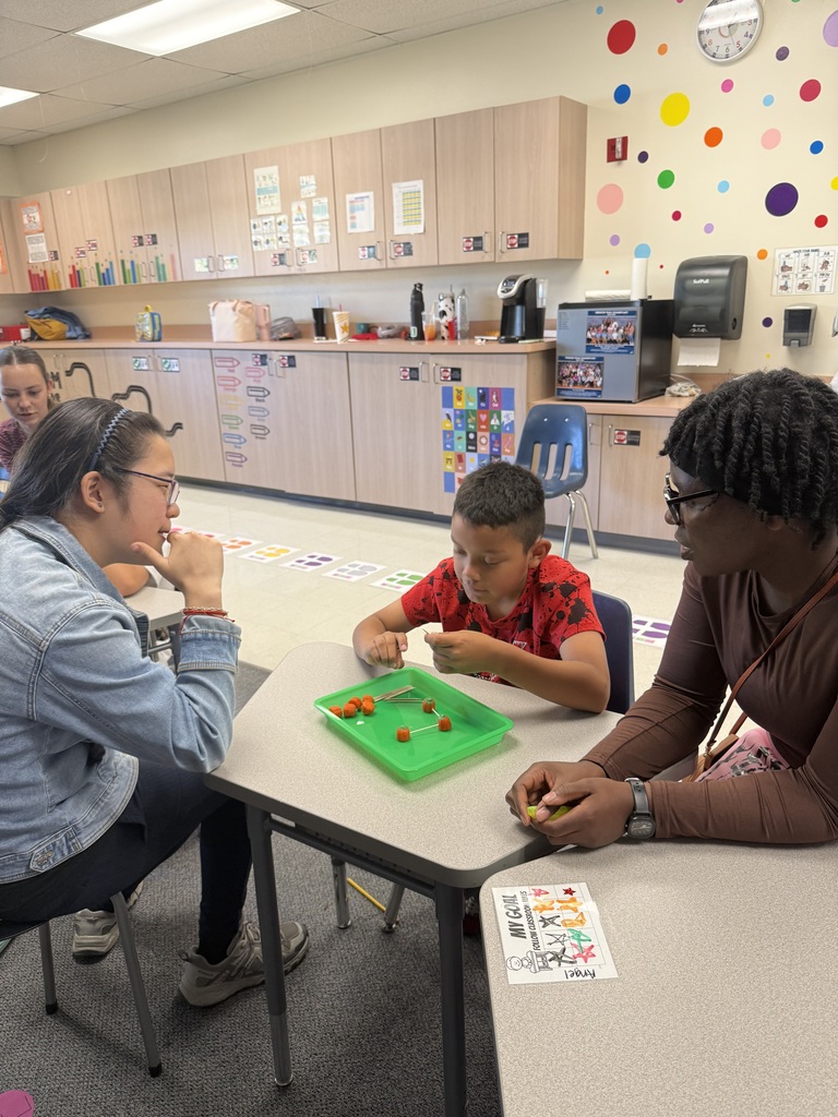 Three people sit around a table, with one child playing with green pieces on a tray.