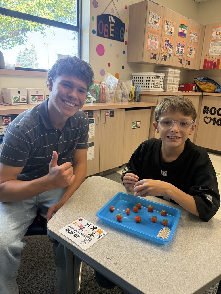 Two boys sitting at a table, one with a thumbs-up, playing with objects on a blue tray.