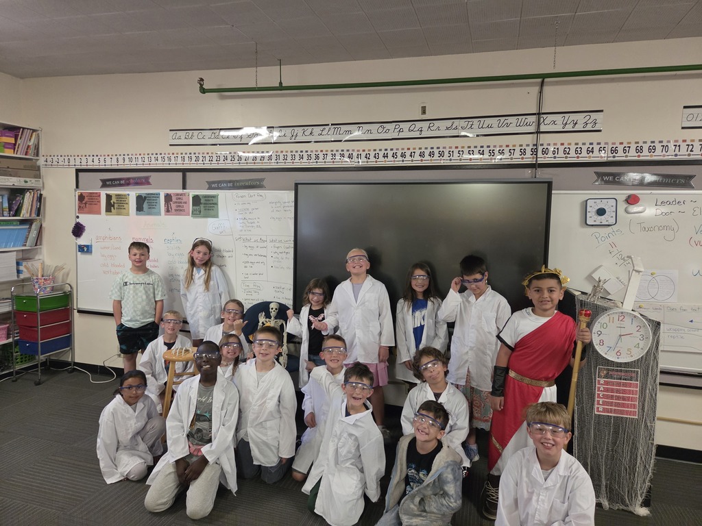 A group of children in white lab coats posing for a photo in a classroom.