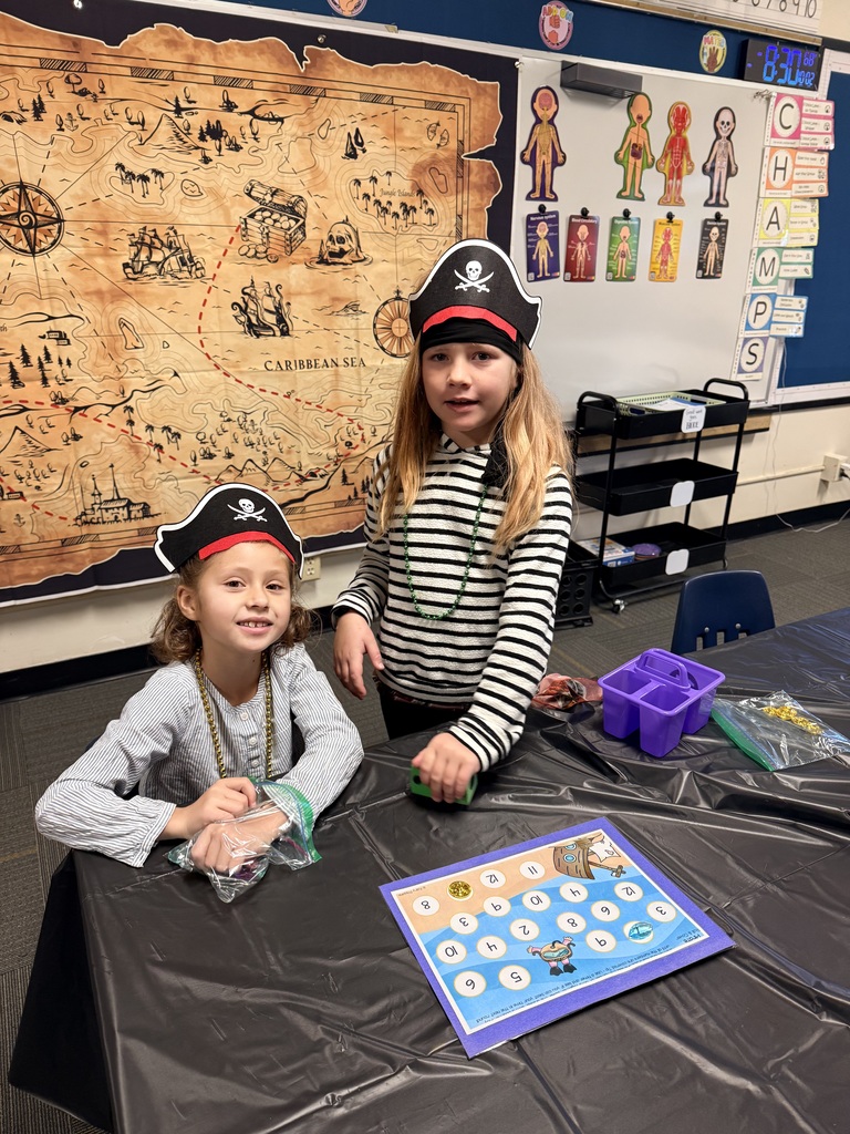 Two children in pirate hats at a table with a pirate map and a board game.