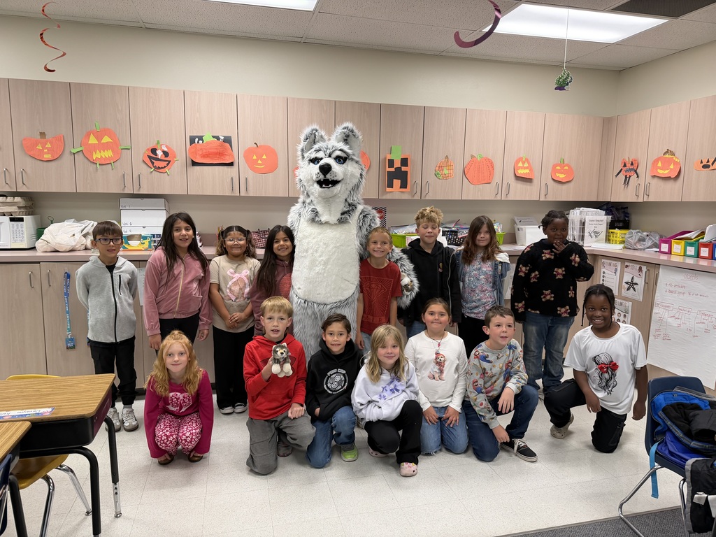 A classroom with children and a mascot dressed as a wolf posing for a group photo.