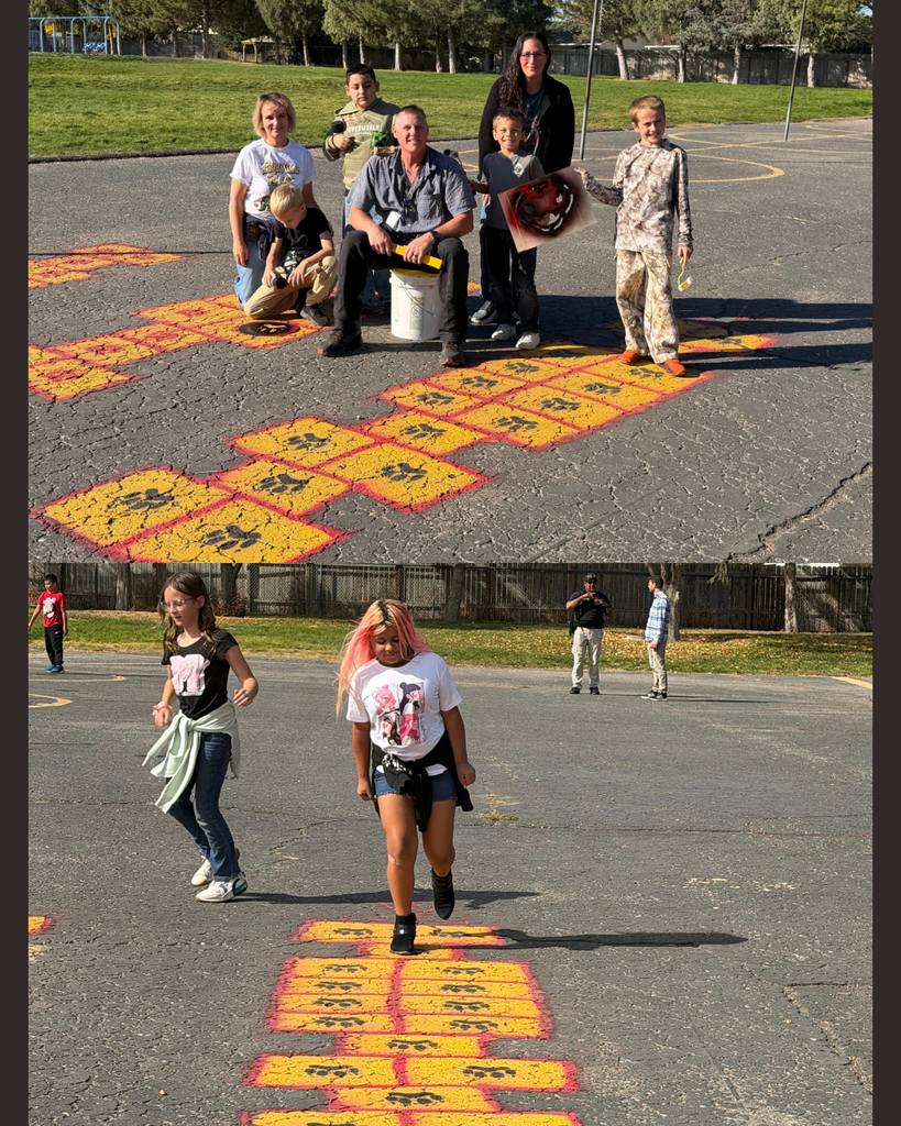 A group of children and adults in a paved area with painted hopscotch. One child jumps, others watch.