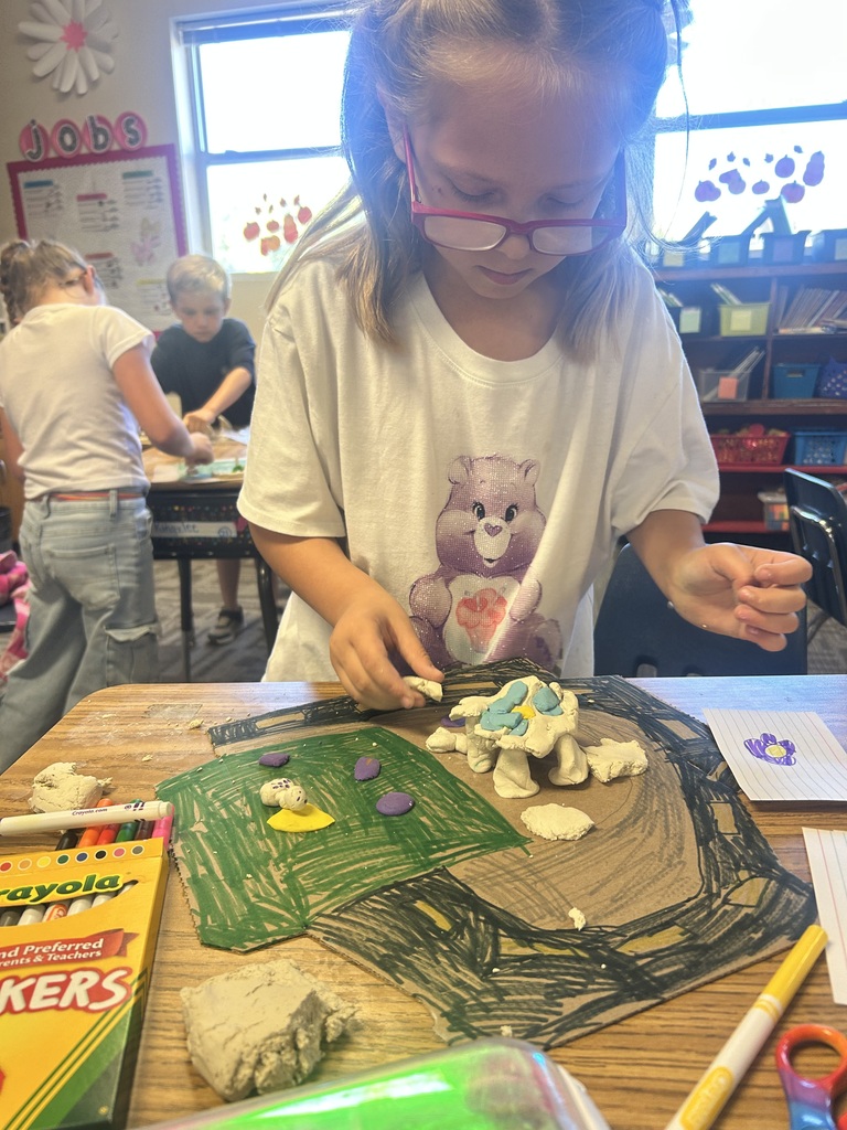 Child in glasses and t-shirt with bear design. She works on a craft project using colored clay.