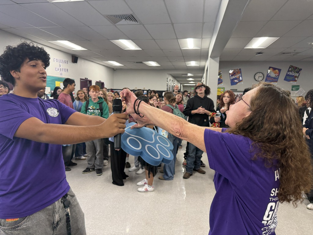Two people in purple shirts interact with each other in a school hallway. Others watch.