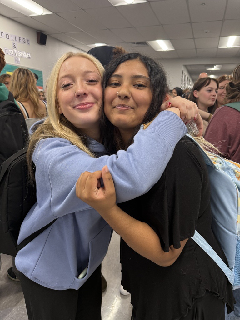 Two women, one with blonde hair and one with dark hair, embrace each other in a hallway.