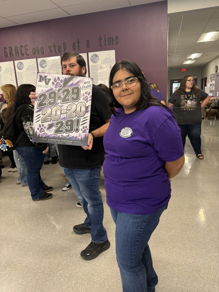 A man and woman pose with a purple sign with numbers and text. They stand in a hall.