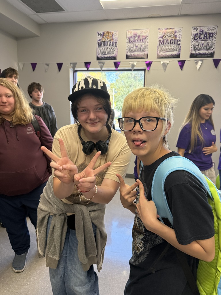 Two kids posing for a photo with peace signs in a hallway with other students.