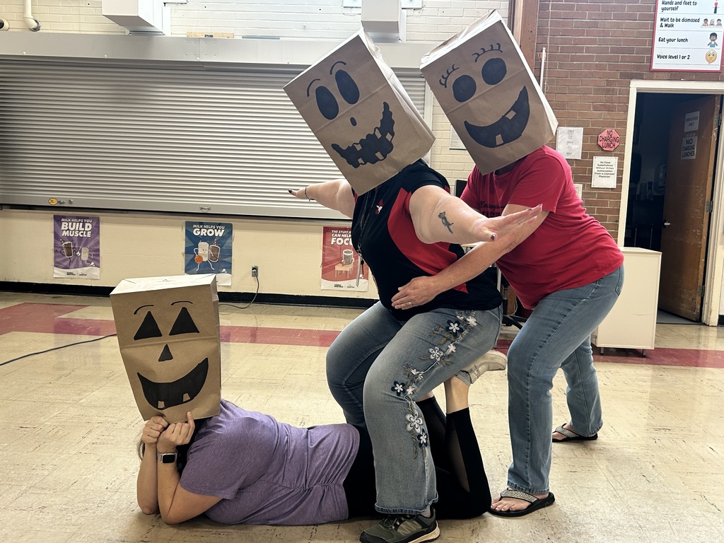 Three people wearing paper masks with faces drawn on them. One person is lying on the ground.