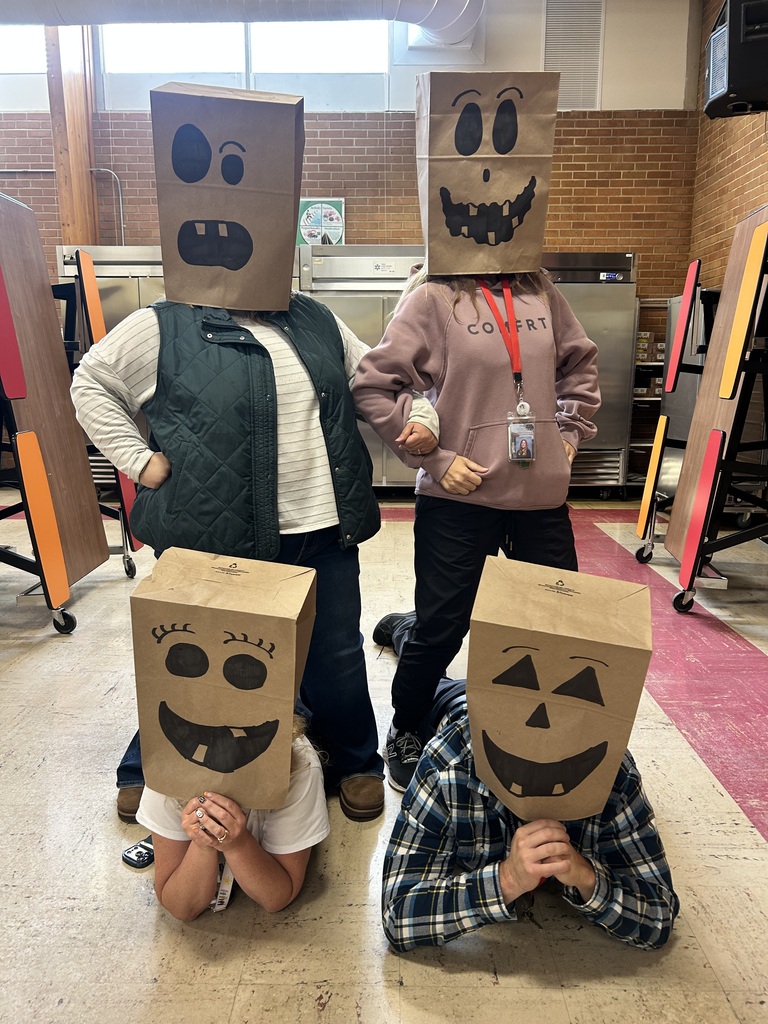 Four people wear cardboard boxes on their heads with faces drawn on them, smiling and showing teeth.