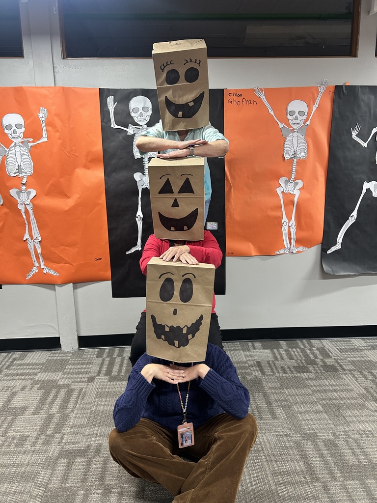 Three people in costume, each wearing a paper bag with a painted face, one with a pumpkin face and two with jack-o-lantern faces.
