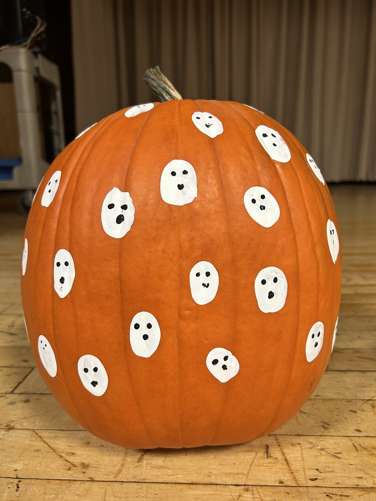 Pumpkin with white faces and eyes painted on an orange background, placed on a wooden floor.