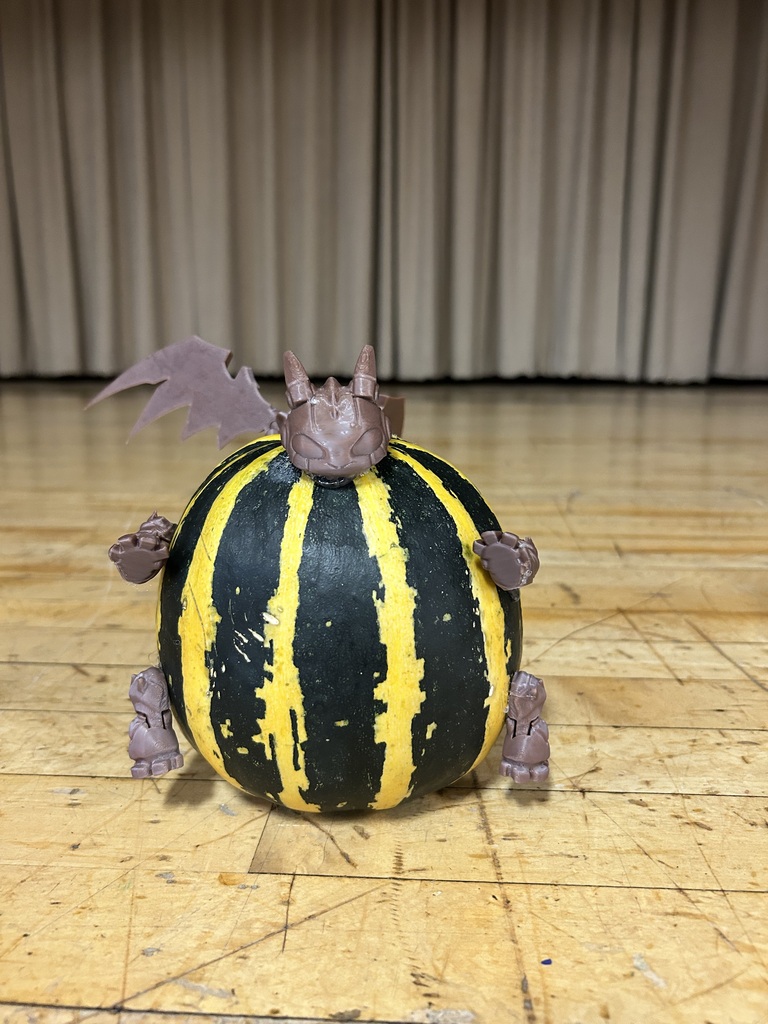 Pumpkin with painted yellow stripes and a bat figurine on top rests on a wooden floor.