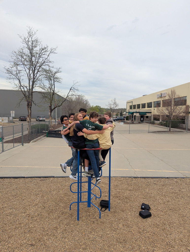 middle school students all gathered on a piece of playground equipment, smiling at the camera