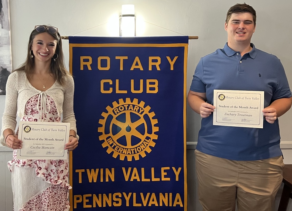 Zachary Troutman and Cecilia Skoniczin holding certificates in front of their rotary club sign 
