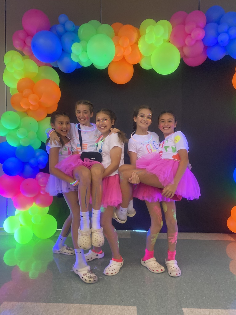 5 girls smiling and posing in pink tutus and crocs under a neon ballon archway