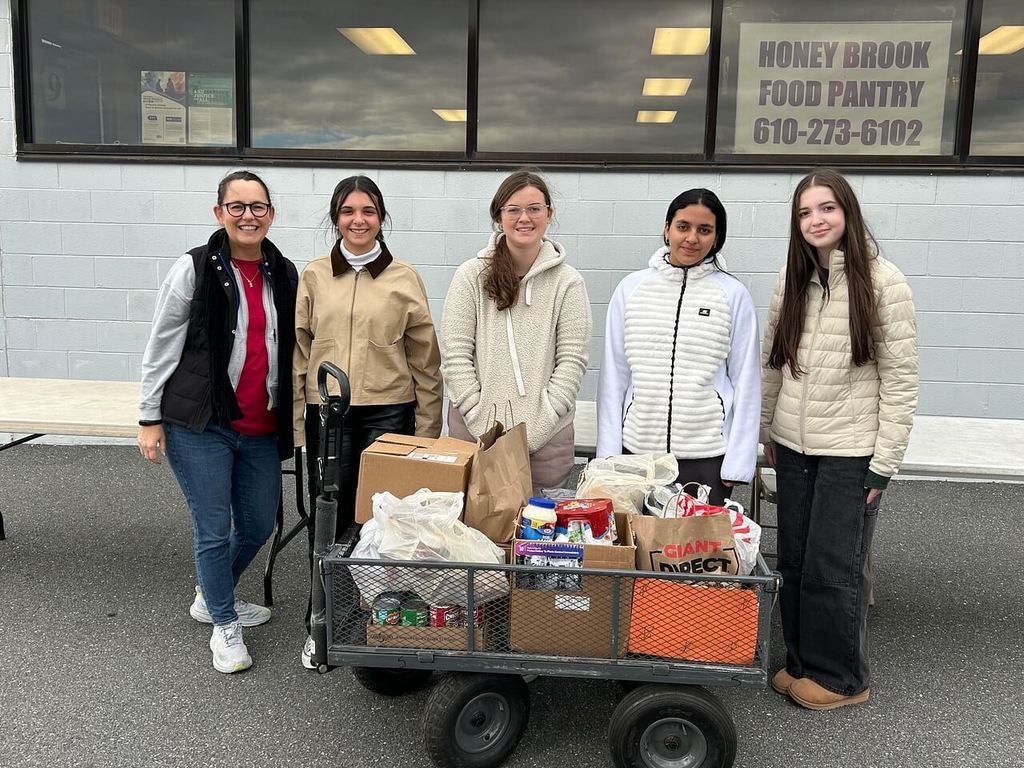 teacher and 4 students standing in front of a wagon filled with food donations