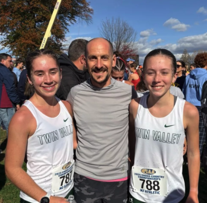 two female runners with their twin valley uniforms smile with their male track and field coach in the middle. celebrating victory!