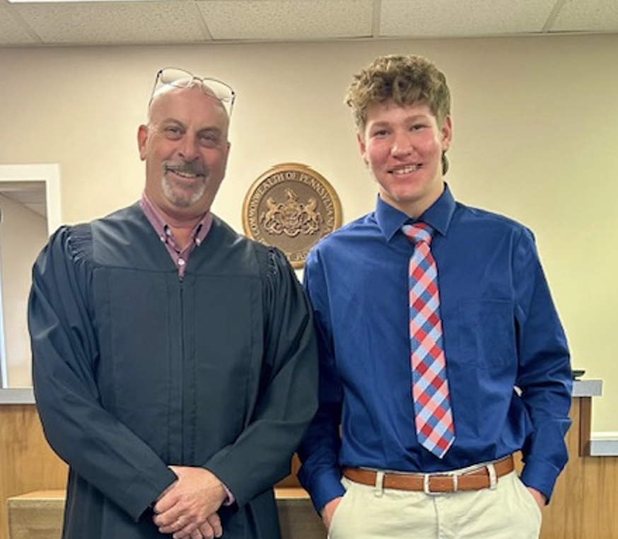 student Caden Siegle smiling next to honorable judge in his robes 