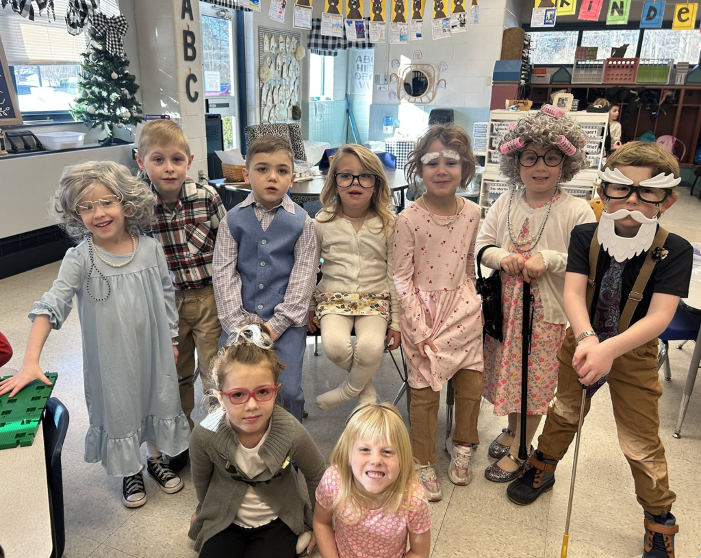 Group of young students dressed up in 'older' garb such as grey beards and wigs, hair rollers, night gowns, and suspenders.