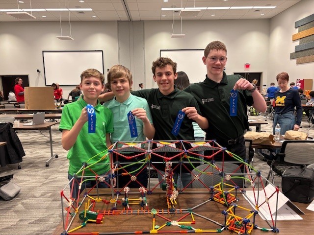 four students holding winning ribbons with k'net structure