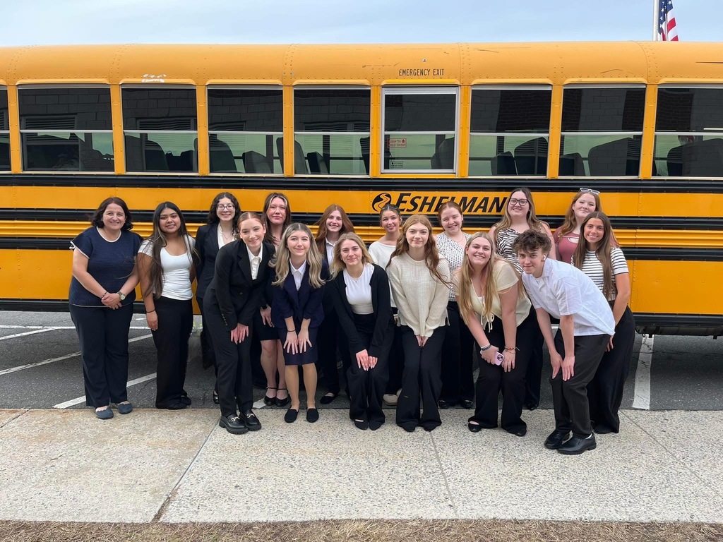 A group of students smiling in front of a yellow school bus