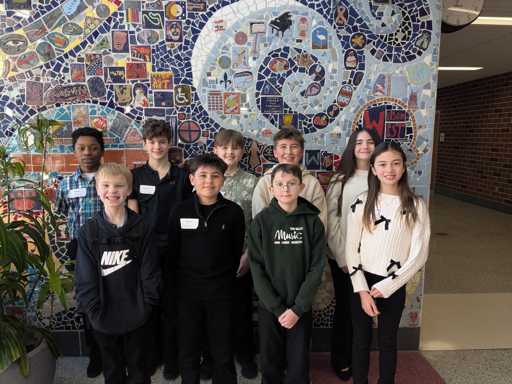 Students smiling in front of mosiac wall