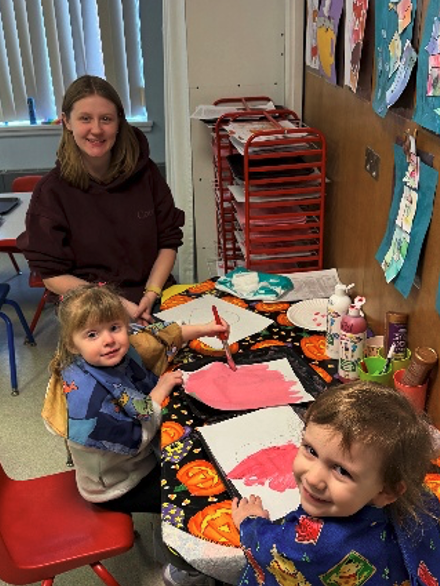 intern smiling with young students who are painting