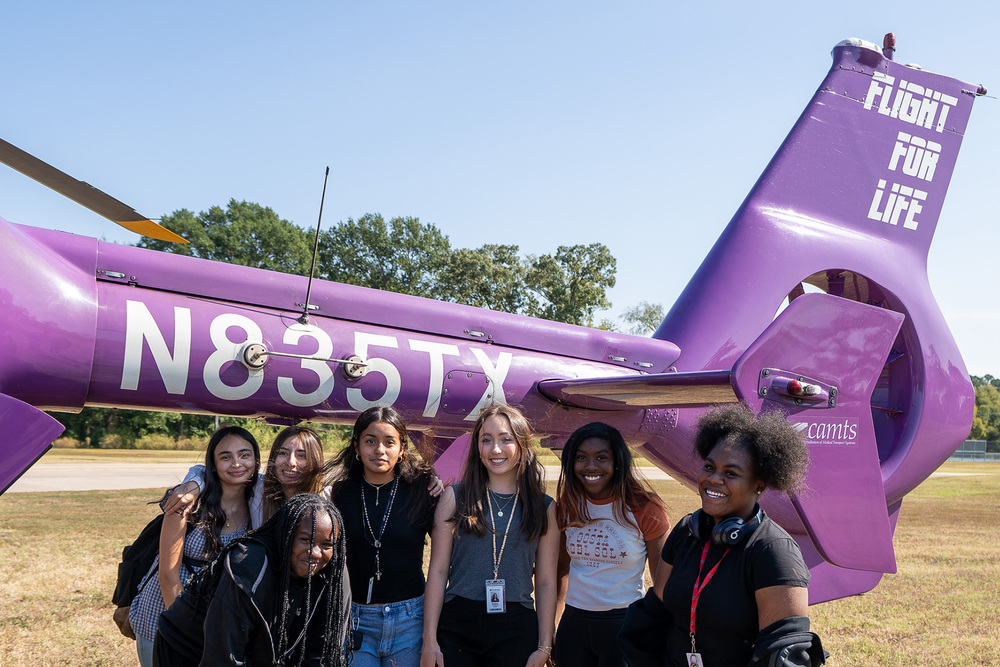 high school girls standing beside a purple helicopter tail