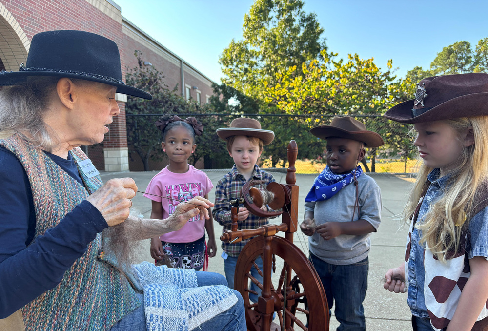 woman showing young kids how to spin llama hair