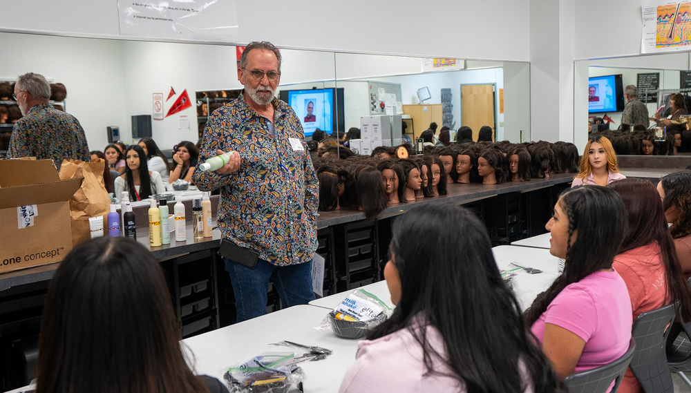 man holding shampoo talks to high school girls in hair salon