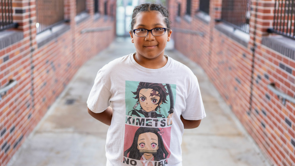 elementary age girl with glasses and a white t-shirt standing in brick walkway