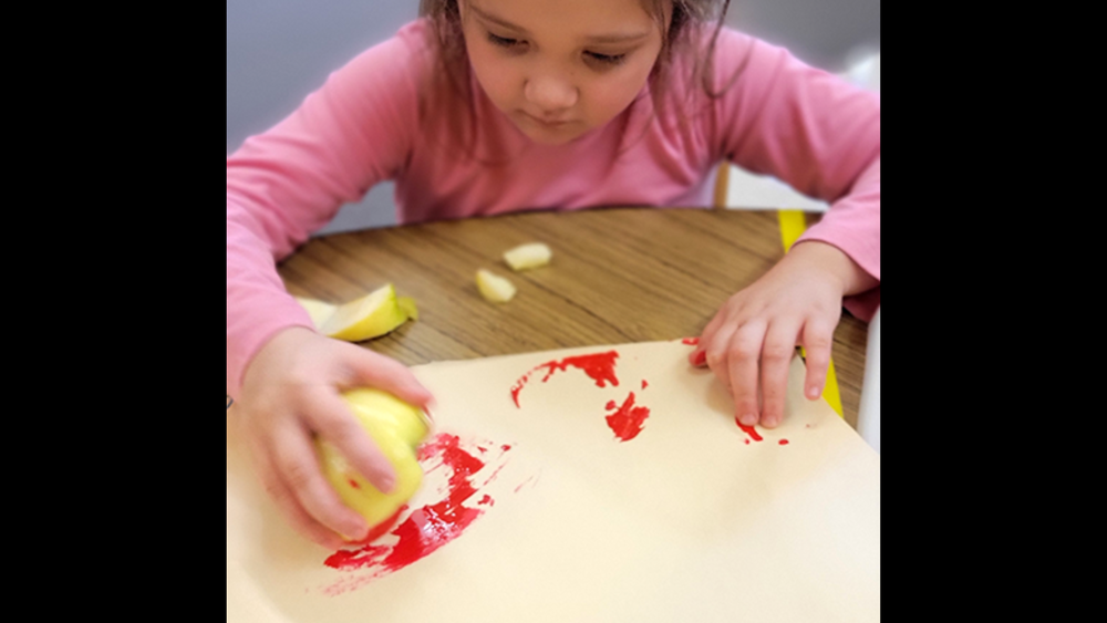 little girl with dark hair is painting with an apple