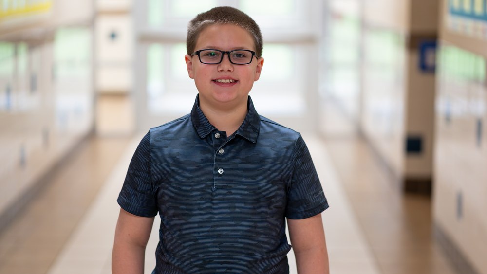 elementary age boy wearing glasses standing in hallway