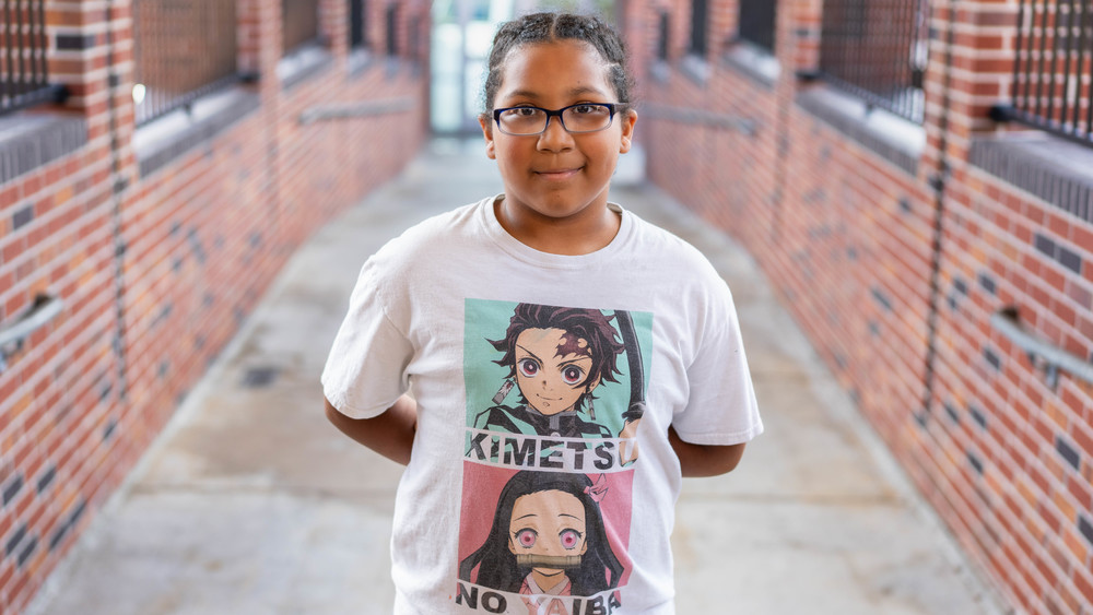 elementary age girl with glasses and a white t-shirt standing in brick walkway