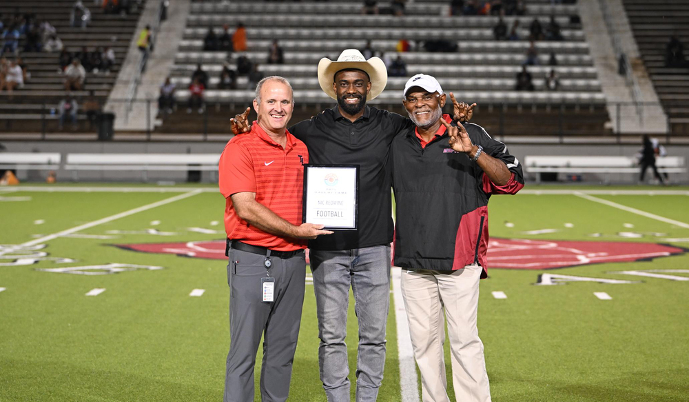Caucasian man standing next to two African American men on a football field