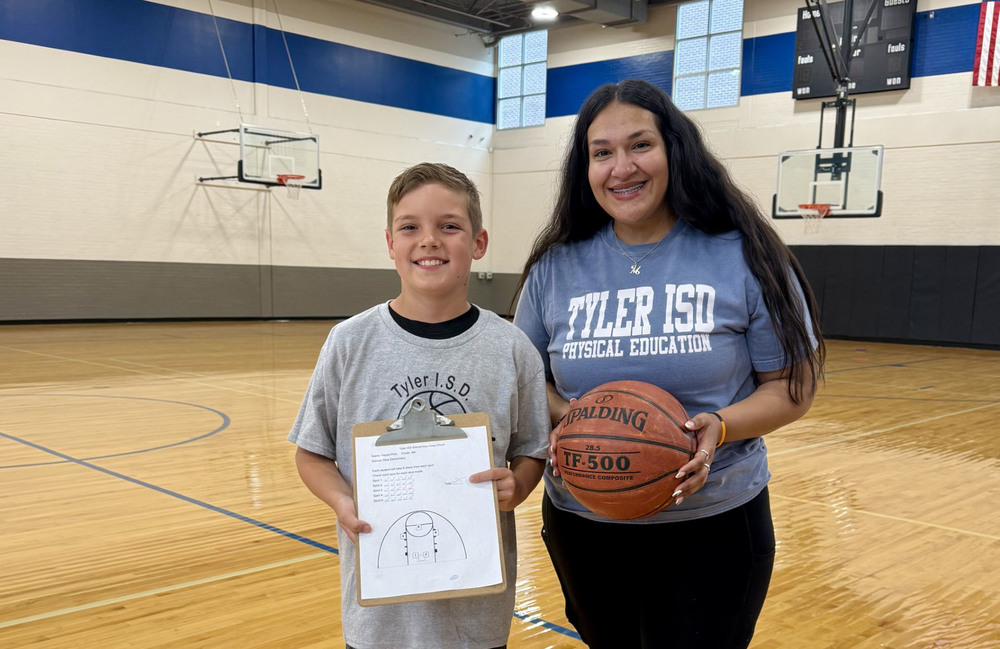 elementary age boy and woman standing in gymnasium with basketball and clipboard