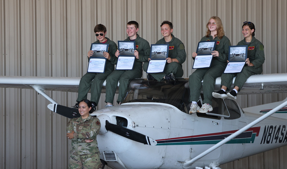 five teen boys and girls sitting on top of small airplane holding certificates