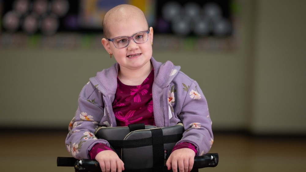 elementary age girl with bald head and glasses smiling