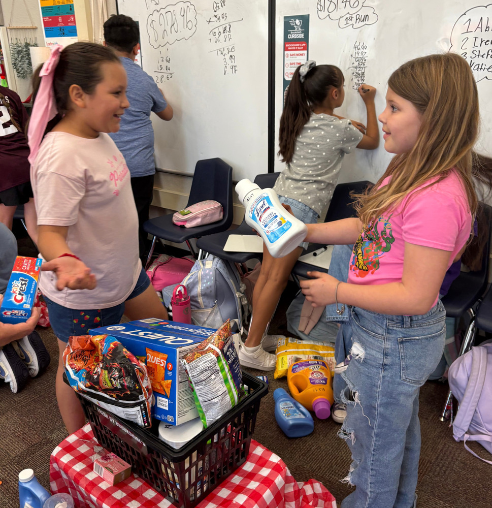 Young girls stand in a classroom with grocery store items.