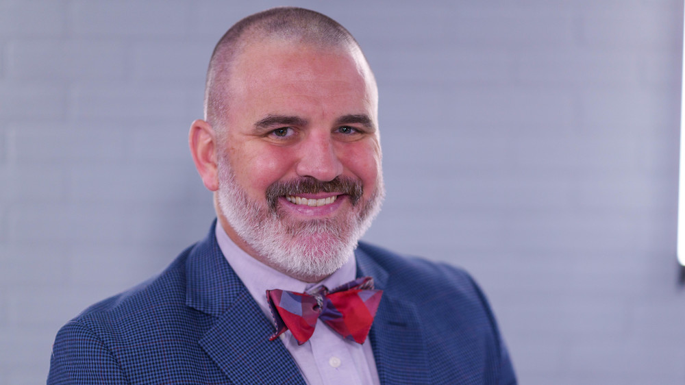 man with beard wearing blue suit jacket and red bow tie smiling big